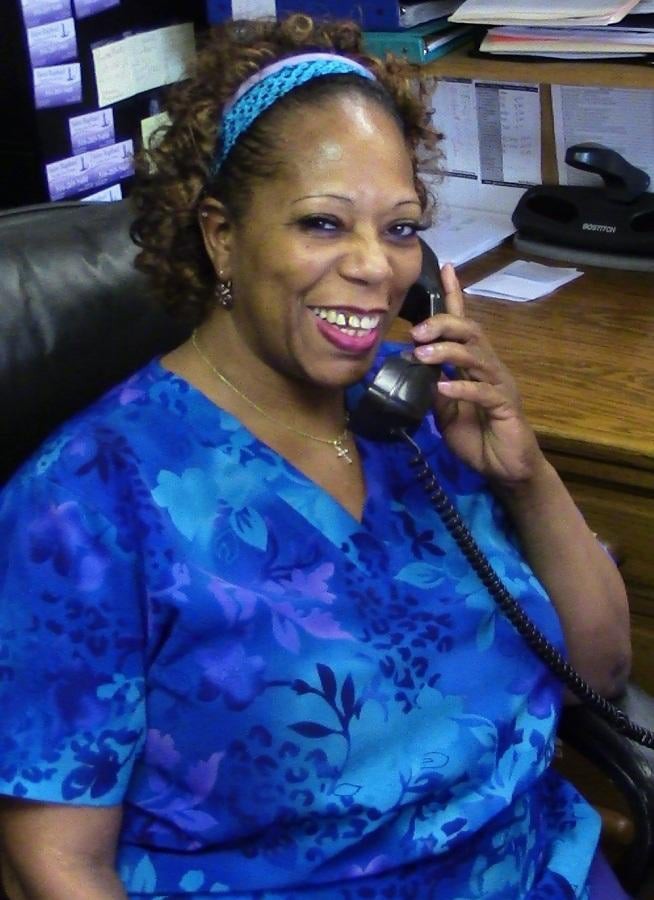 A woman in a blue shirt smiling while on the phone in an office setting.