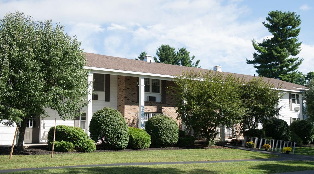A suburban apartment building with a brick facade, surrounded by trees and shrubs.