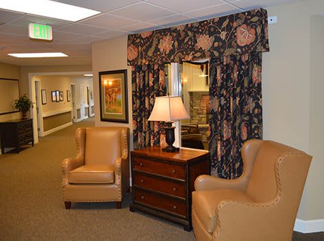 A cozy lounge area featuring two leather chairs, a wooden table with a lamp, and decorative curtains.