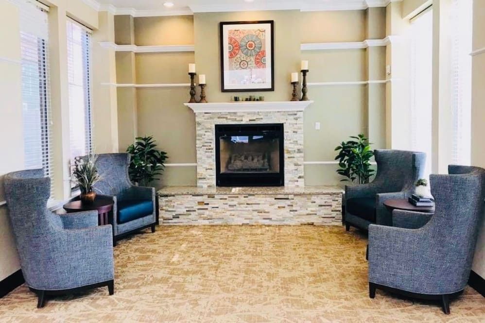 A cozy living room with a central fireplace, surrounded by elegant chairs and decorated with indoor plants and framed art.