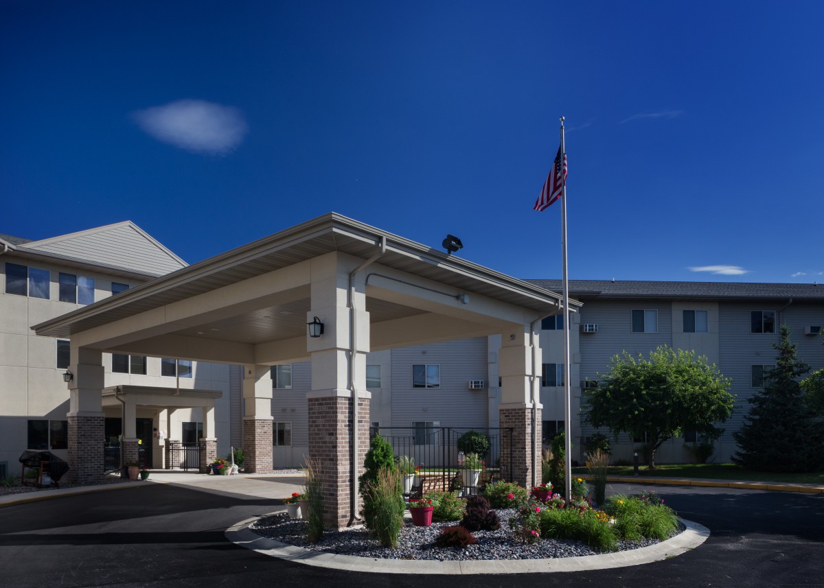A building with a covered entrance and a flagpole, surrounded by landscaping under a clear blue sky.