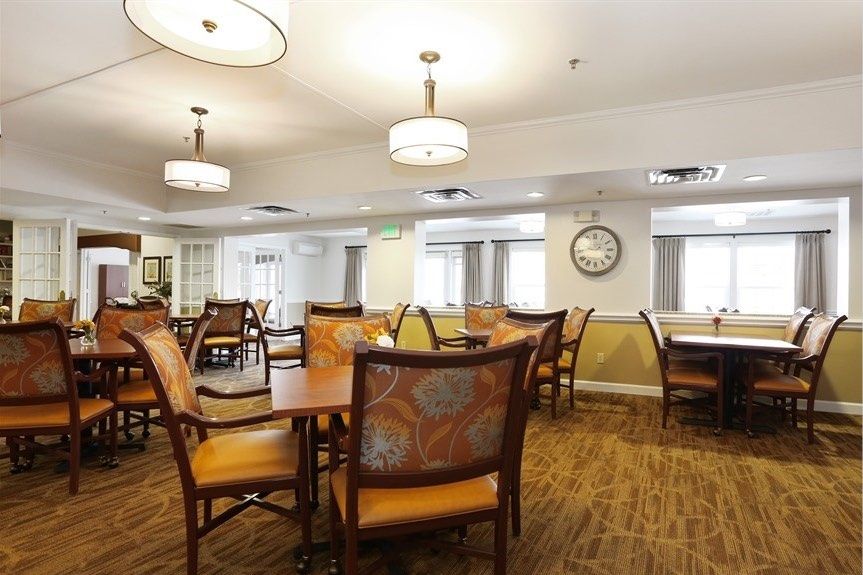 A spacious dining area with neatly arranged tables and chairs, complemented by warm lighting and wooden flooring.