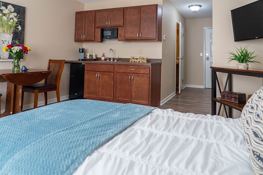 A modern hotel room featuring a bed, kitchenette, and desk area.