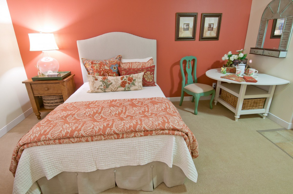 A cozy bedroom with a bed adorned in patterned bedding, featuring a small side table with a lamp and decorative items.