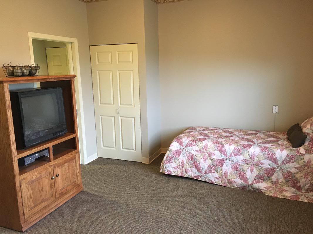 A simple bedroom with a bed, television, and minimal furnishings.
