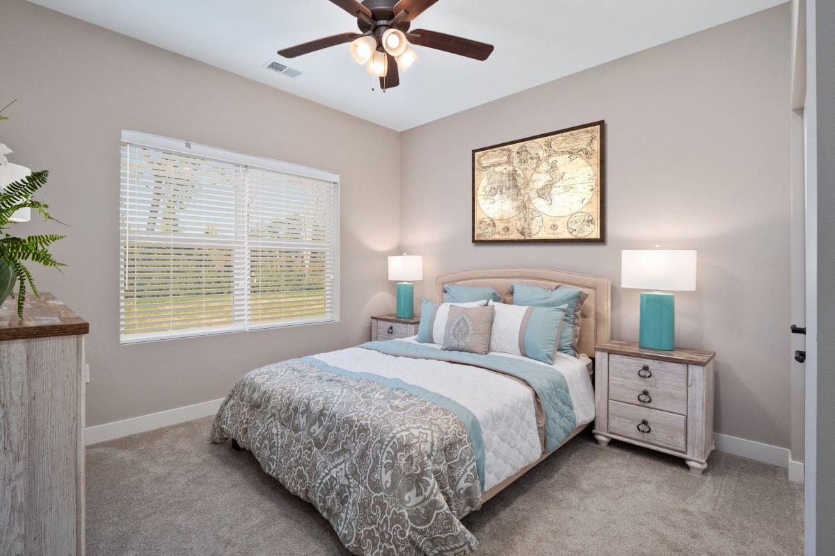 A cozy bedroom with a neatly made double bed, accentuated by bedside tables and lamps, featuring wall artwork and a ceiling fan.