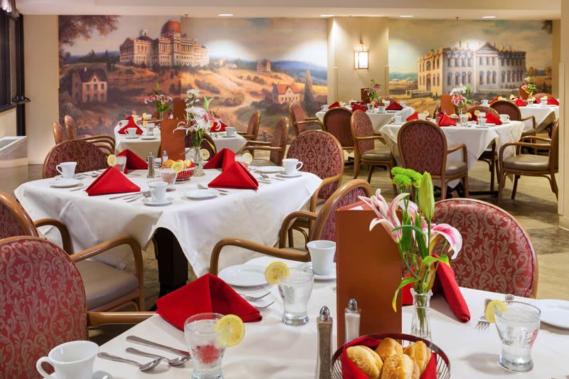 An elegant restaurant dining area with neatly arranged tables, adorned with red napkins and floral centerpieces.