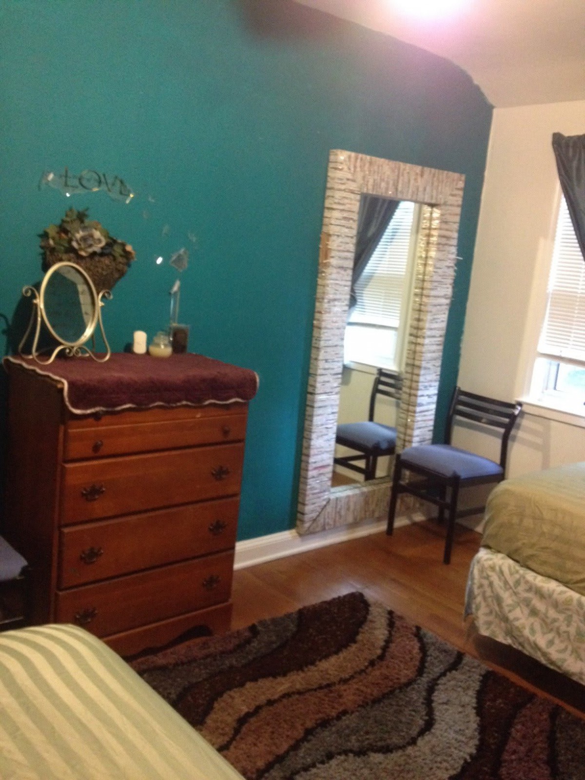 A cozy bedroom featuring a wooden dresser, a tall mirror, and a comfortable chair by the window.