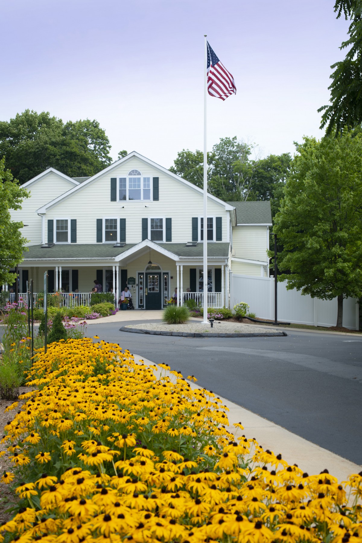 A large white building with a landscaped garden of yellow flowers and an American flag flying on a flagpole at the entrance.