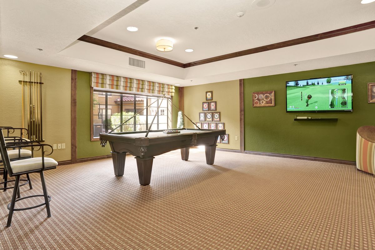 A well-lit game room featuring a pool table and a television on the wall.