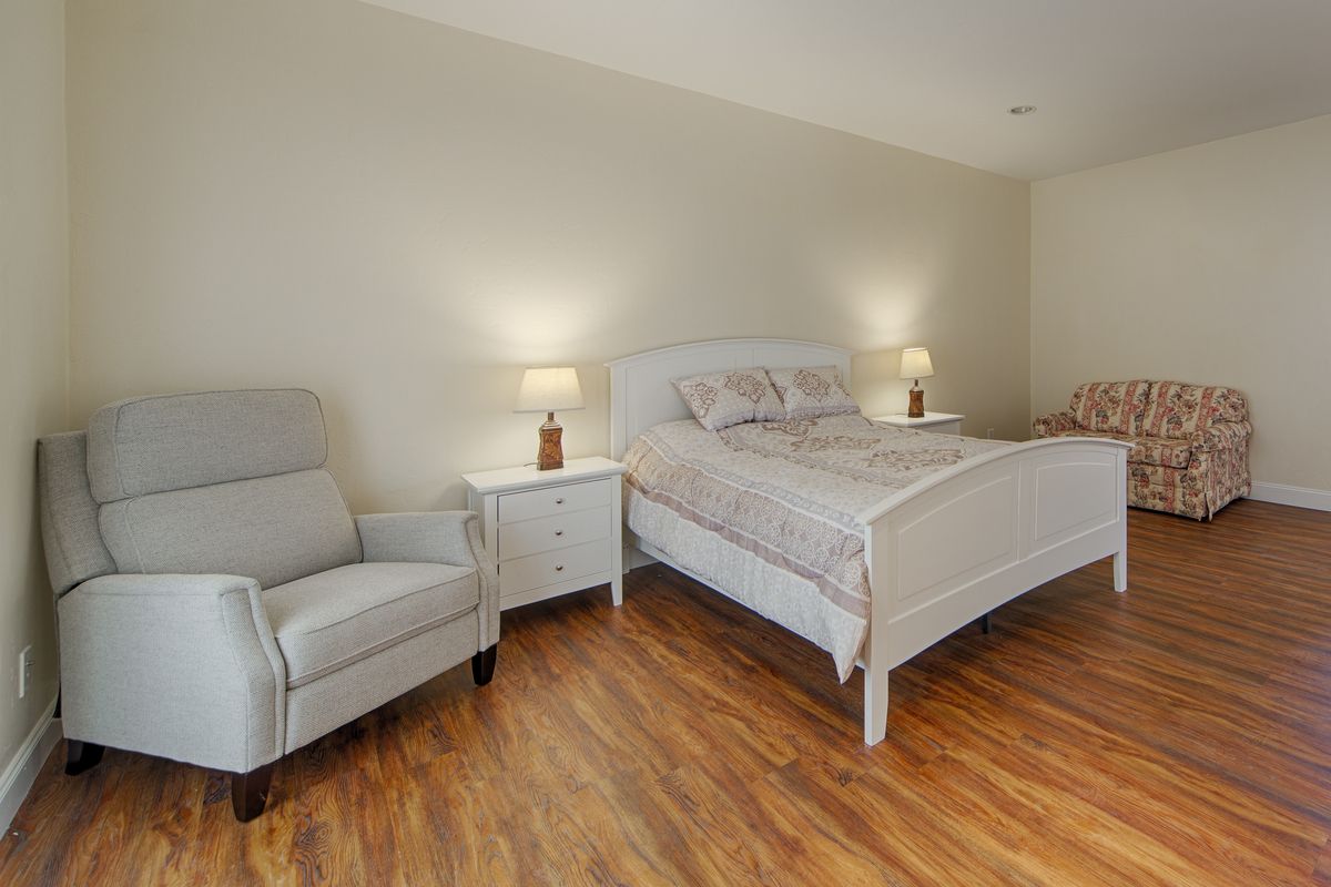 A cozy bedroom featuring a comfortable bed with a nightstand on each side, accompanied by an armchair and warm lighting.