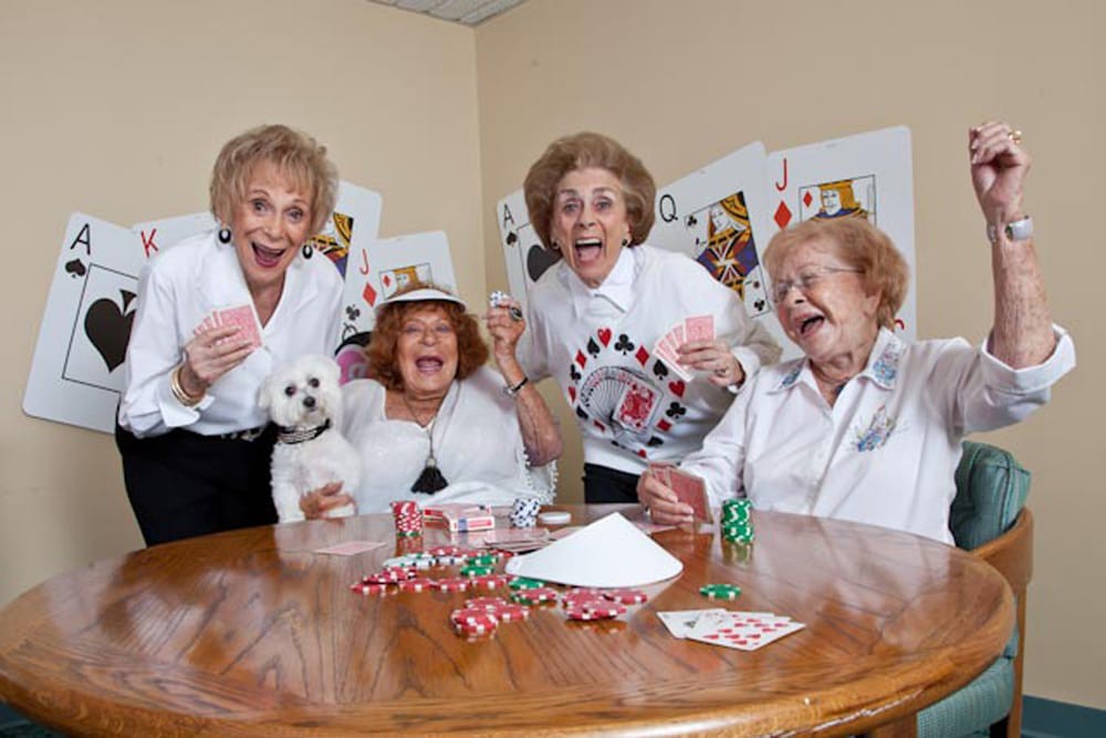 Four elderly women joyfully playing cards together, accompanied by a small dog.