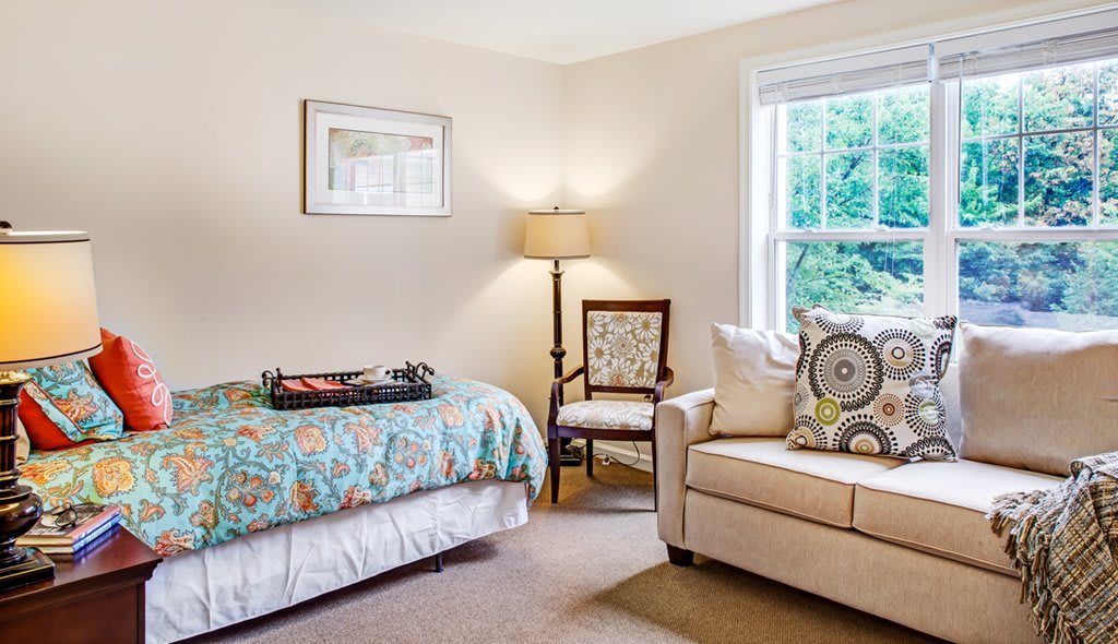 Cozy bedroom with a bed, chair, lamp, and couch near a window.