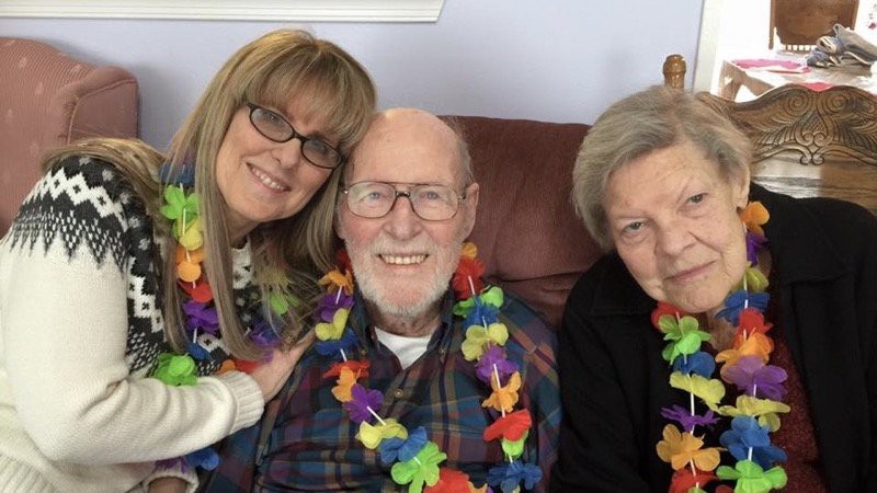A group of three people wearing colorful leis and smiling indoors.