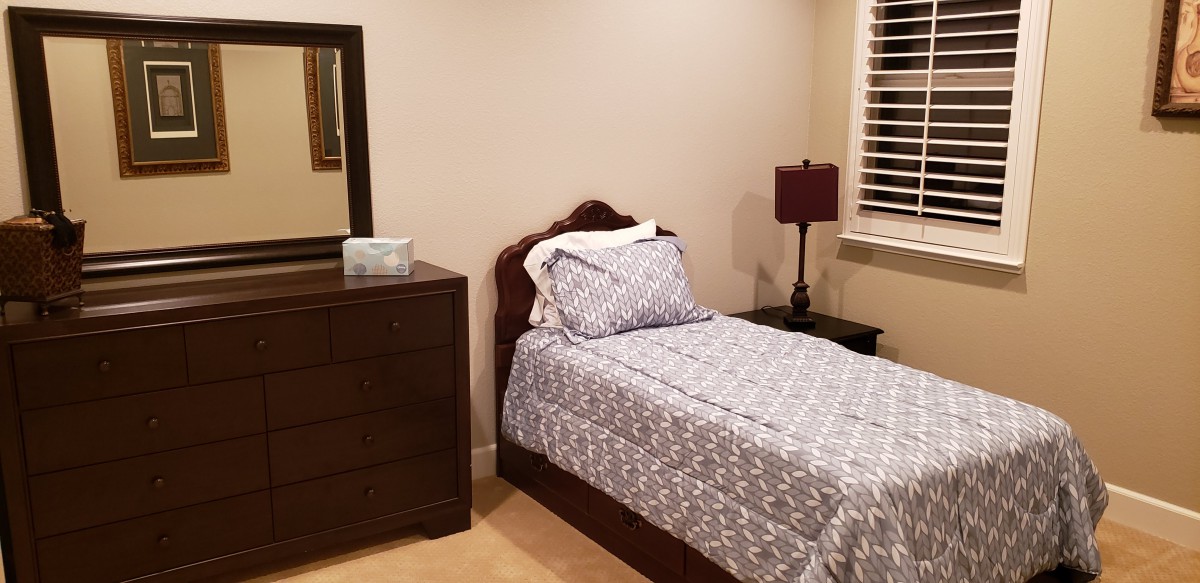 A neatly arranged bedroom with a single bed, dresser, and nightstand.