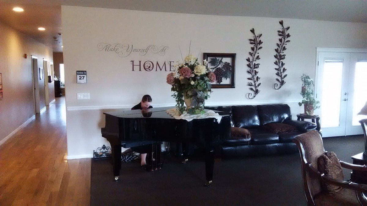 A cozy living room featuring a grand piano with a floral arrangement on top, a leather couch, and decorative wall art.