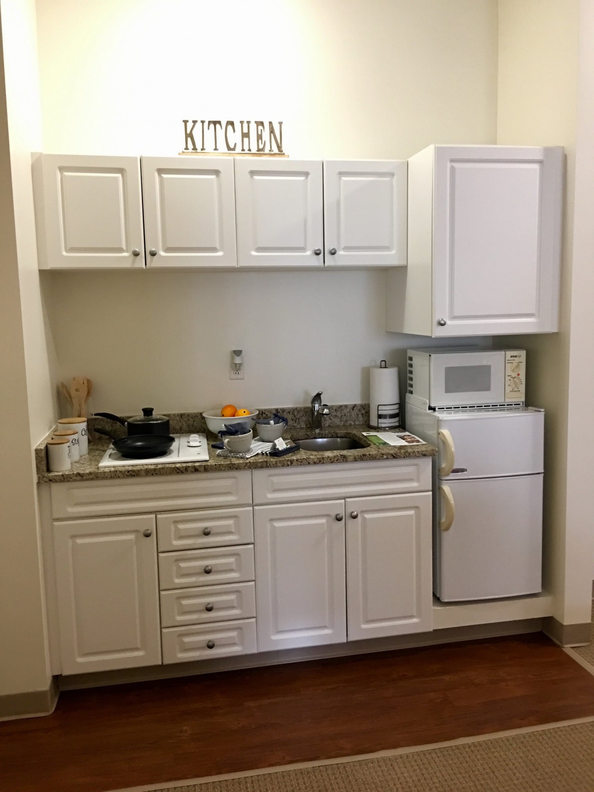 A compact kitchen with white cabinets, a sink, microwave, and small fridge.