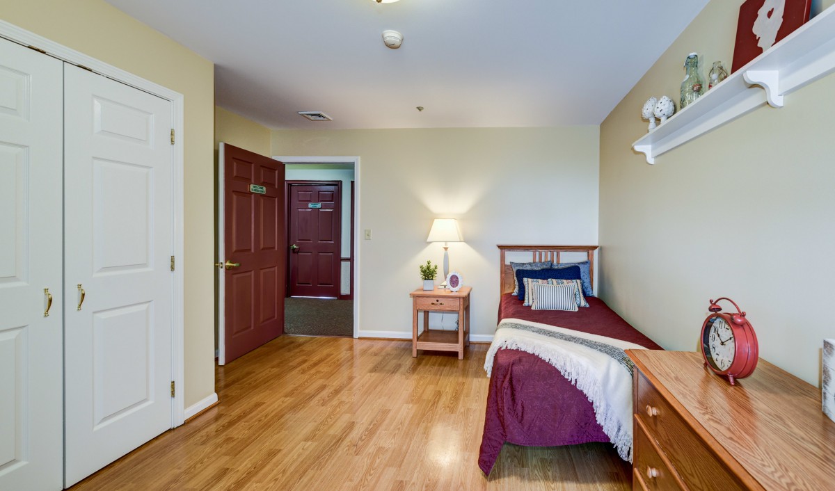 A minimalist bedroom with a single bed and nightstand on a hardwood floor.