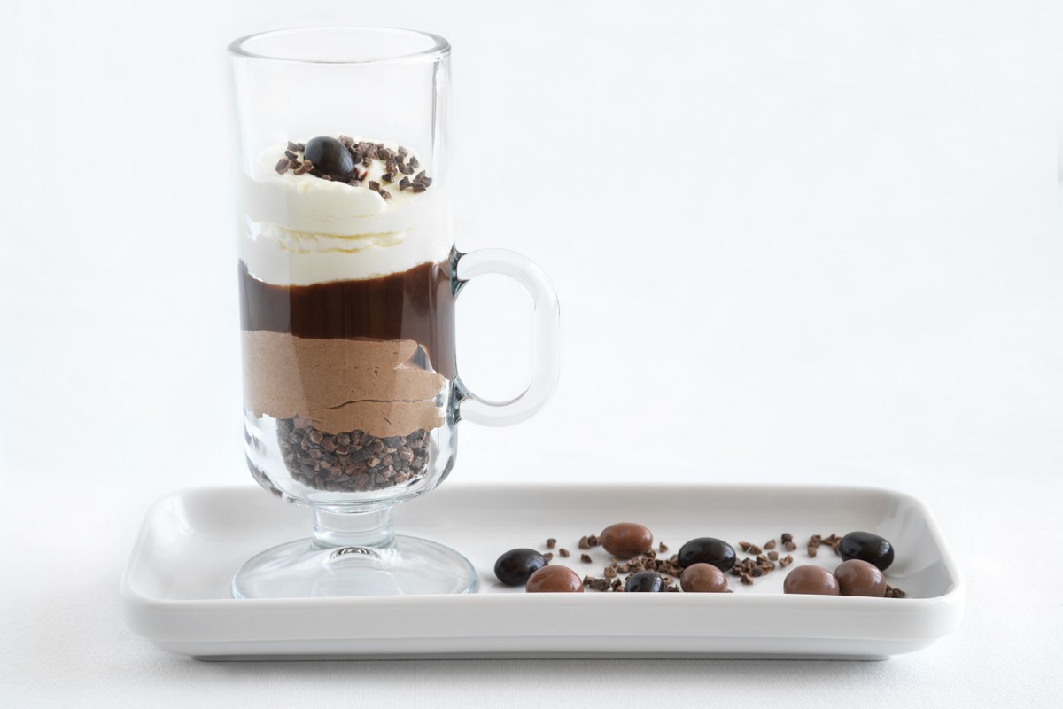 A gourmet layered chocolate dessert served in a glass with a side of assorted chocolates on a plate.