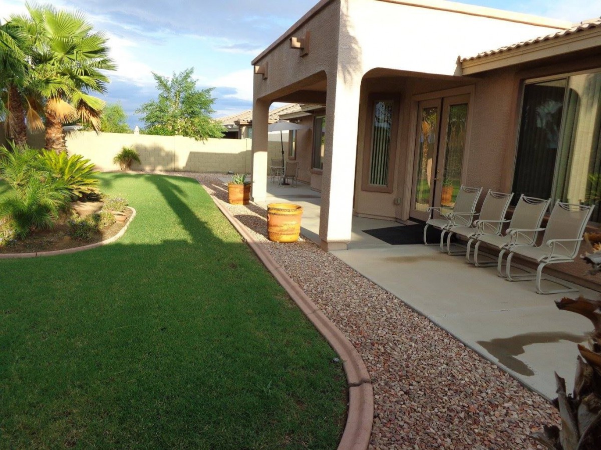 A well-maintained backyard featuring a patio with seating, lush green lawn, and neatly arranged landscaping.