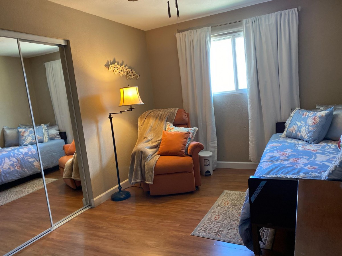A cozy bedroom with a comfortable chair, bed, and a standing lamp near the window.