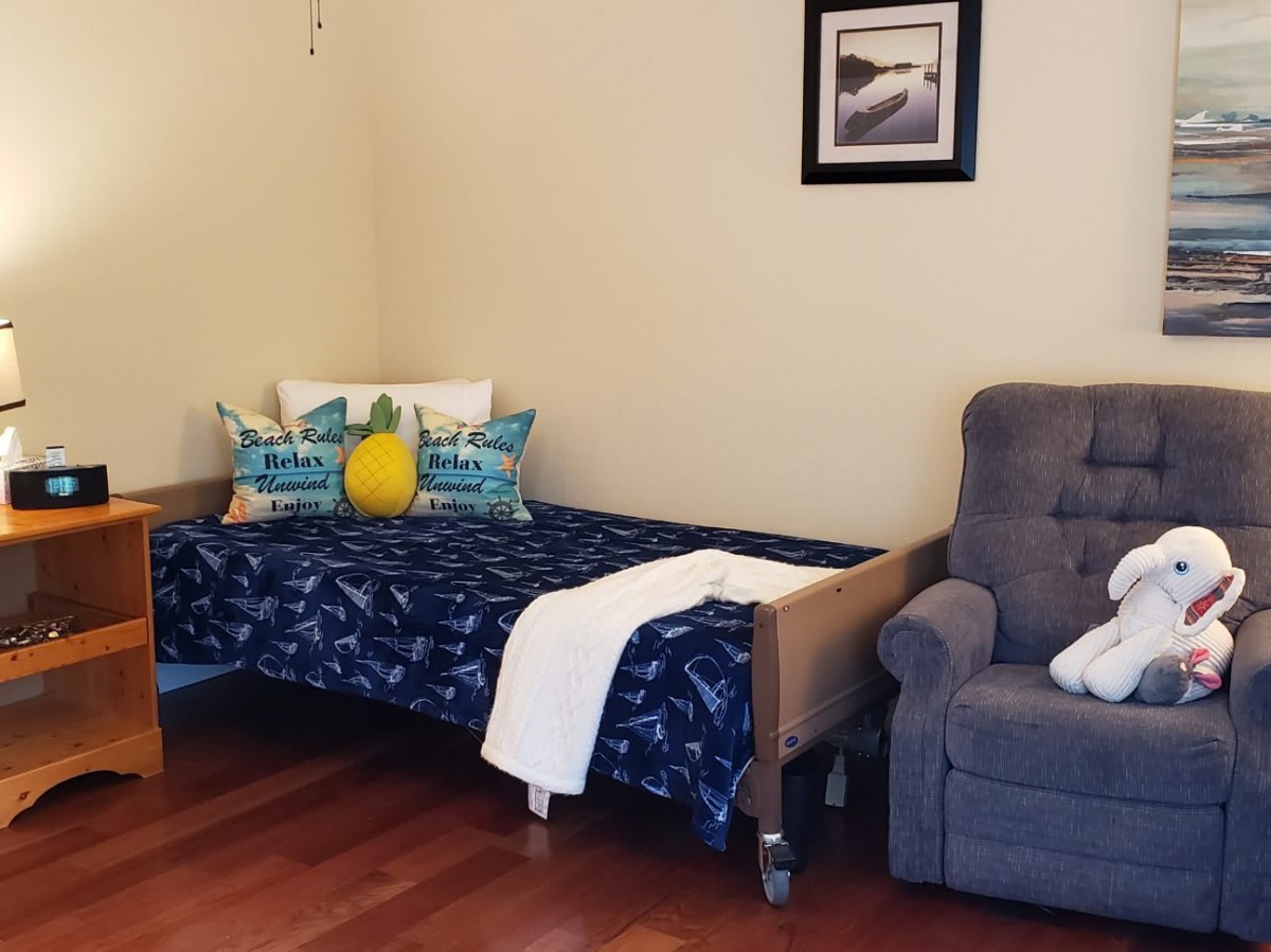 A cozy bedroom with a single bed, armchair, and decorative pillows on a wooden floor.