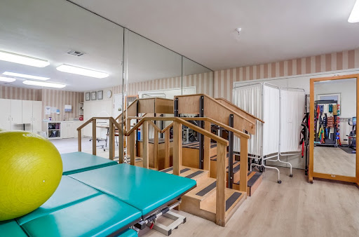 A well-equipped rehabilitation therapy room featuring a set of stairs and treatment tables.