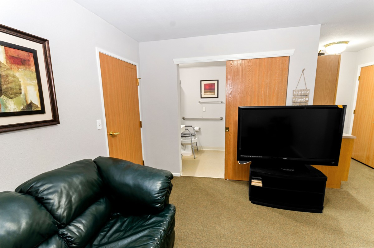 A cozy living room with a leather chair, television, and doors leading to another room.