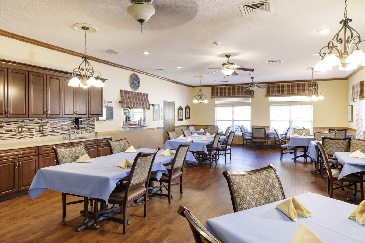 A well-decorated dining area with neatly arranged tables and chairs, illuminated by ceiling lights and natural light from the windows.