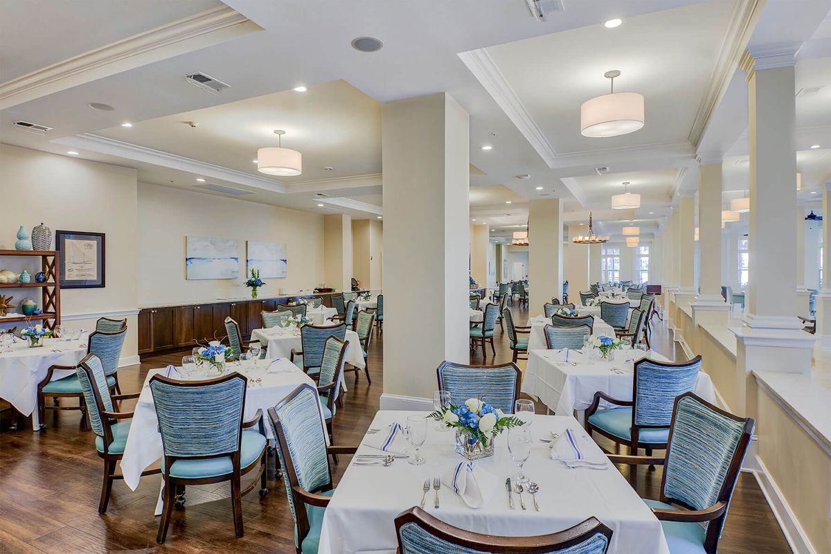 An elegantly set dining room with neatly arranged tables and chairs, featuring soft lighting.