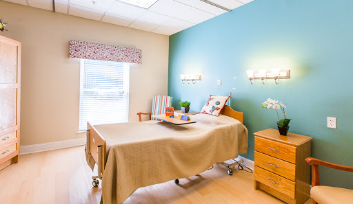 A well-lit hospital patient room featuring a bed, nightstand, and decorative touches for comfort.