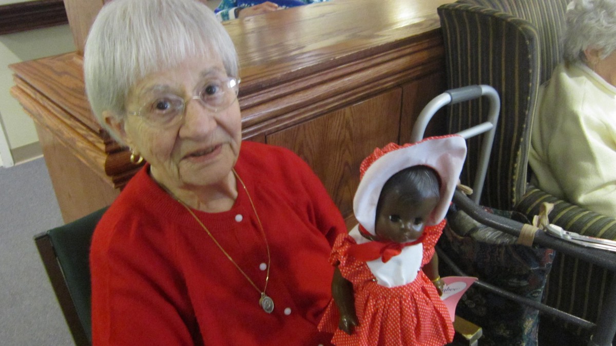 An elderly woman in red holding a doll inside a room.
