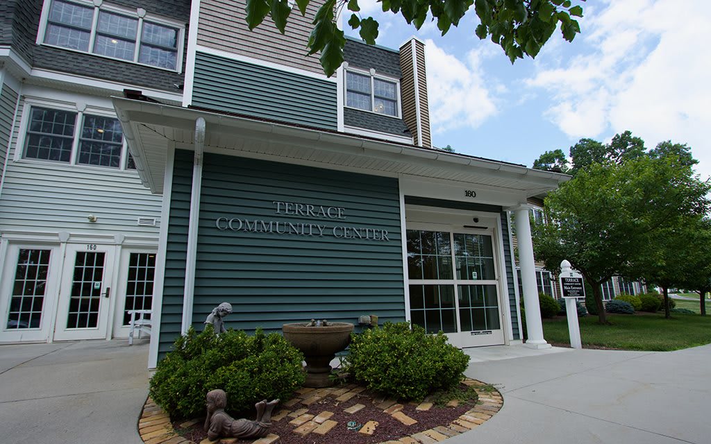 Front entrance of a public library with green siding and surrounding landscaping.