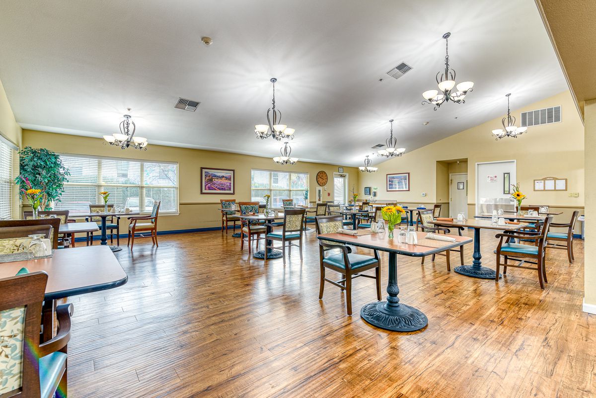 A bright and spacious dining room with neatly arranged tables and chairs, featuring wooden floors and chandeliers.