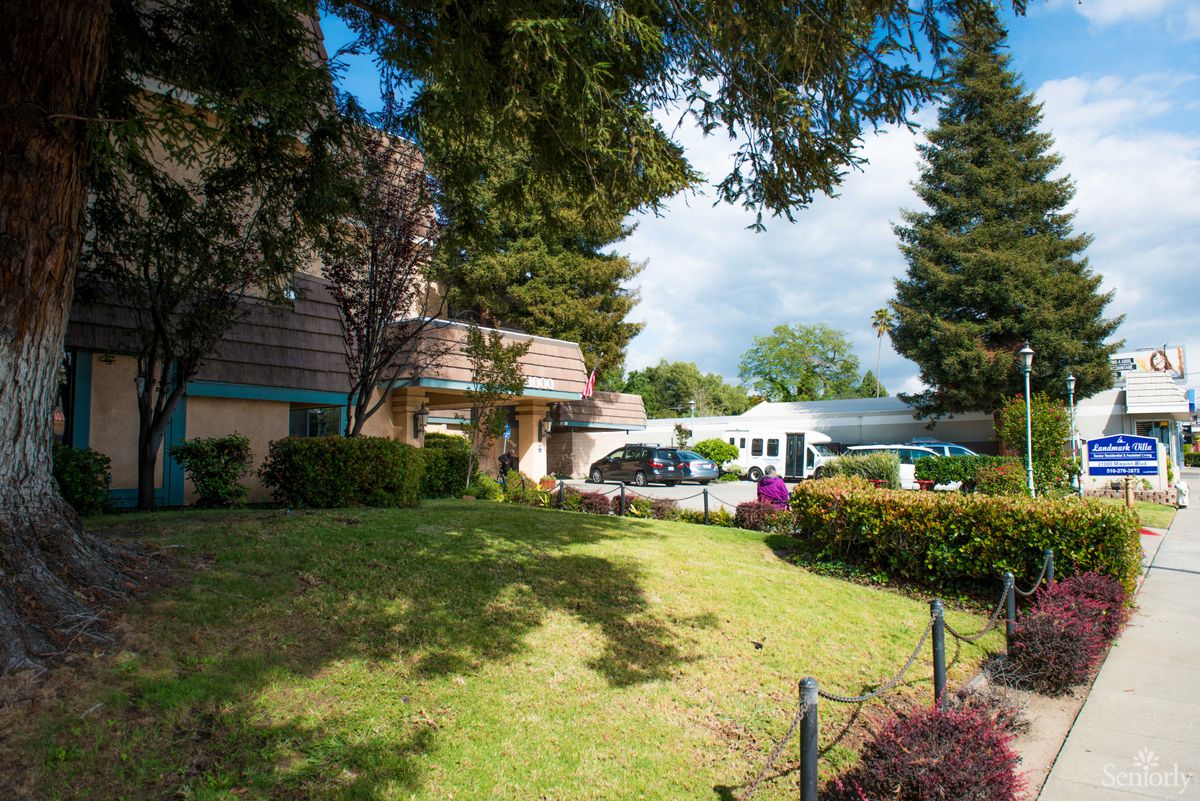 A scenic view of a building surrounded by trees and a well-maintained lawn, with cars parked nearby.