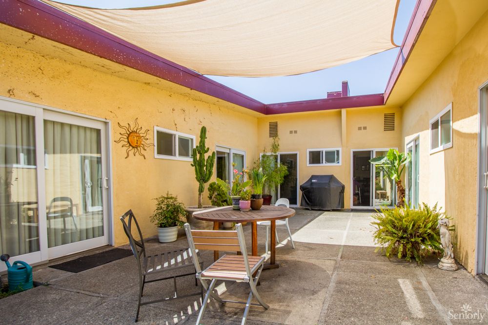 A sunny courtyard with a table and chairs, surrounded by potted plants, under a shade sail.