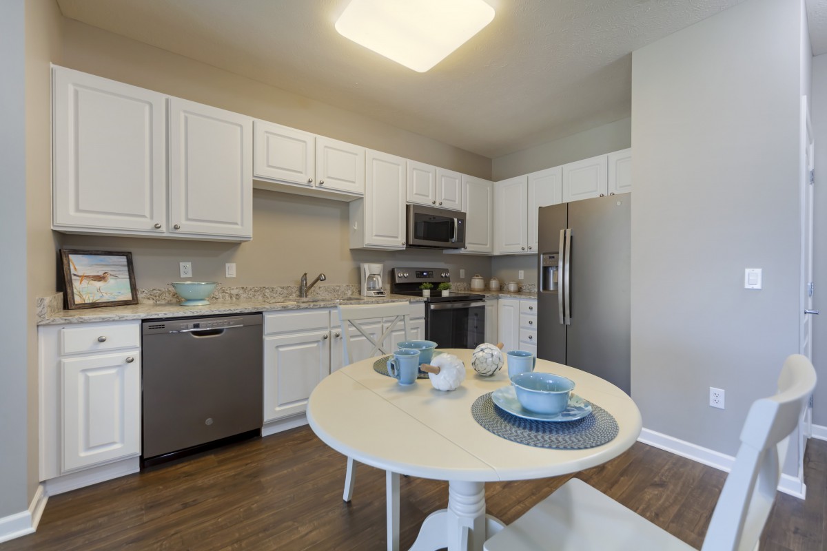 A modern kitchen with white cabinets and a small dining table set under bright lighting.