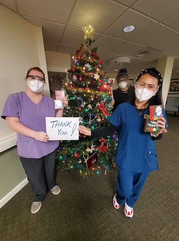 Healthcare workers express gratitude during the holiday season in front of a beautifully decorated Christmas tree.