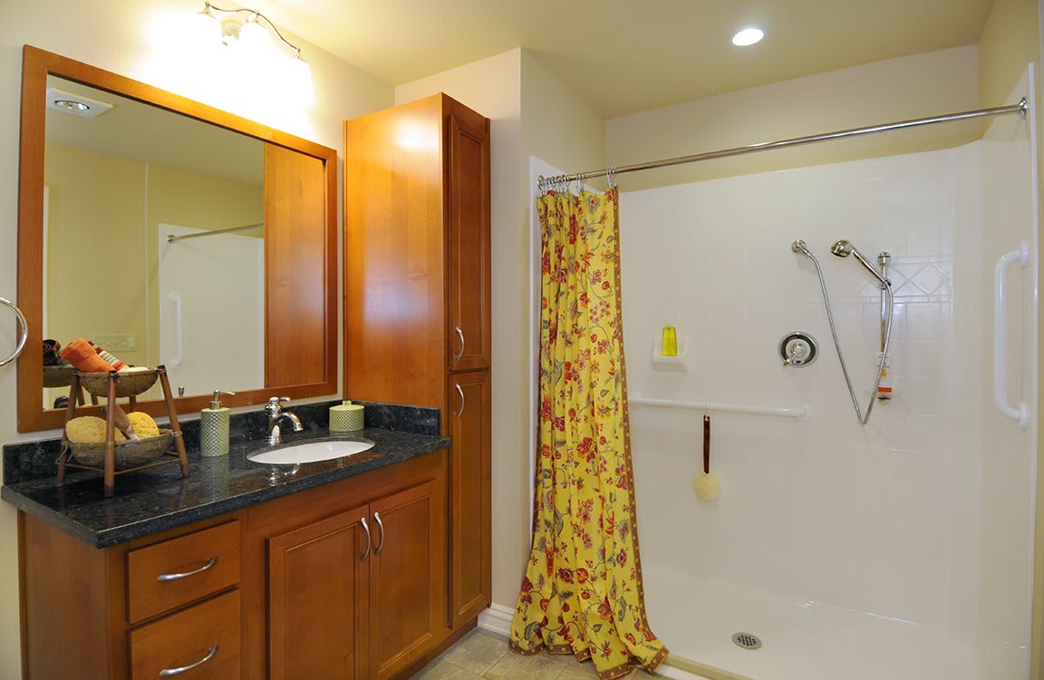 A well-lit bathroom featuring a wooden cabinet, a mirror, and a shower area with a floral curtain.