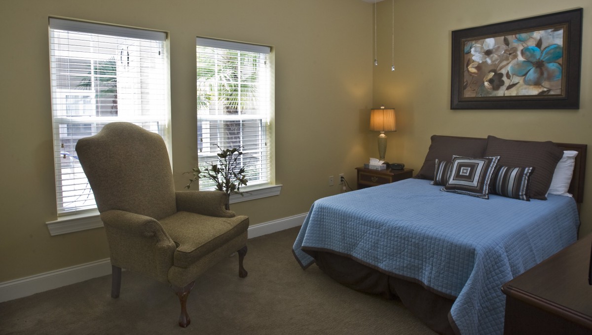 A cozy bedroom with a bed, armchair, and a lamp beside the window.