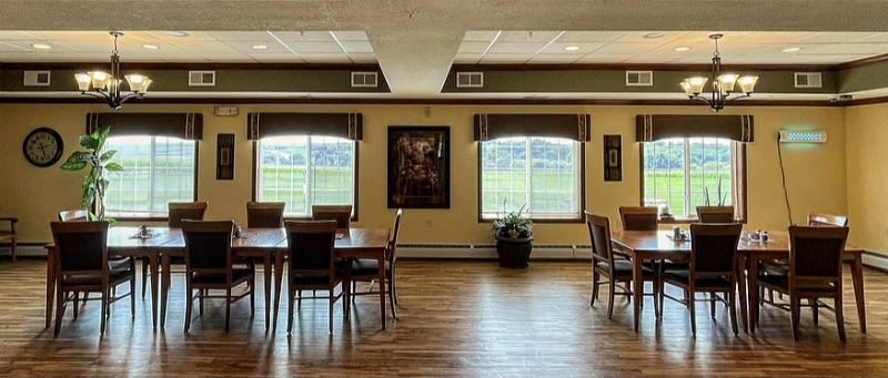 A spacious dining area with wooden tables and chairs, illuminated by natural light from large windows.