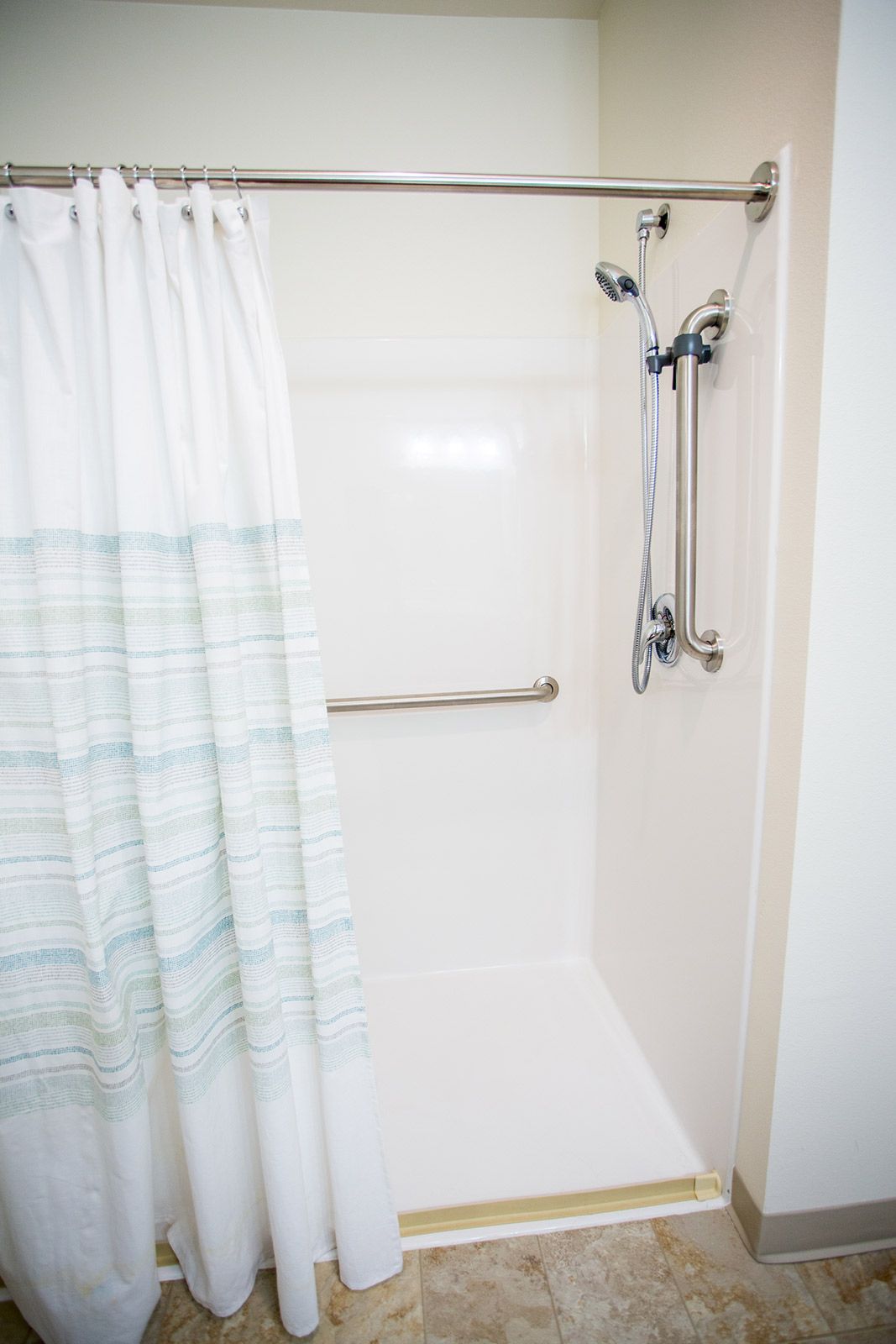 A modern shower with a striped curtain and grab bar.