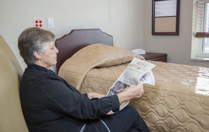 A person sitting on a bed reading a newspaper indoors.