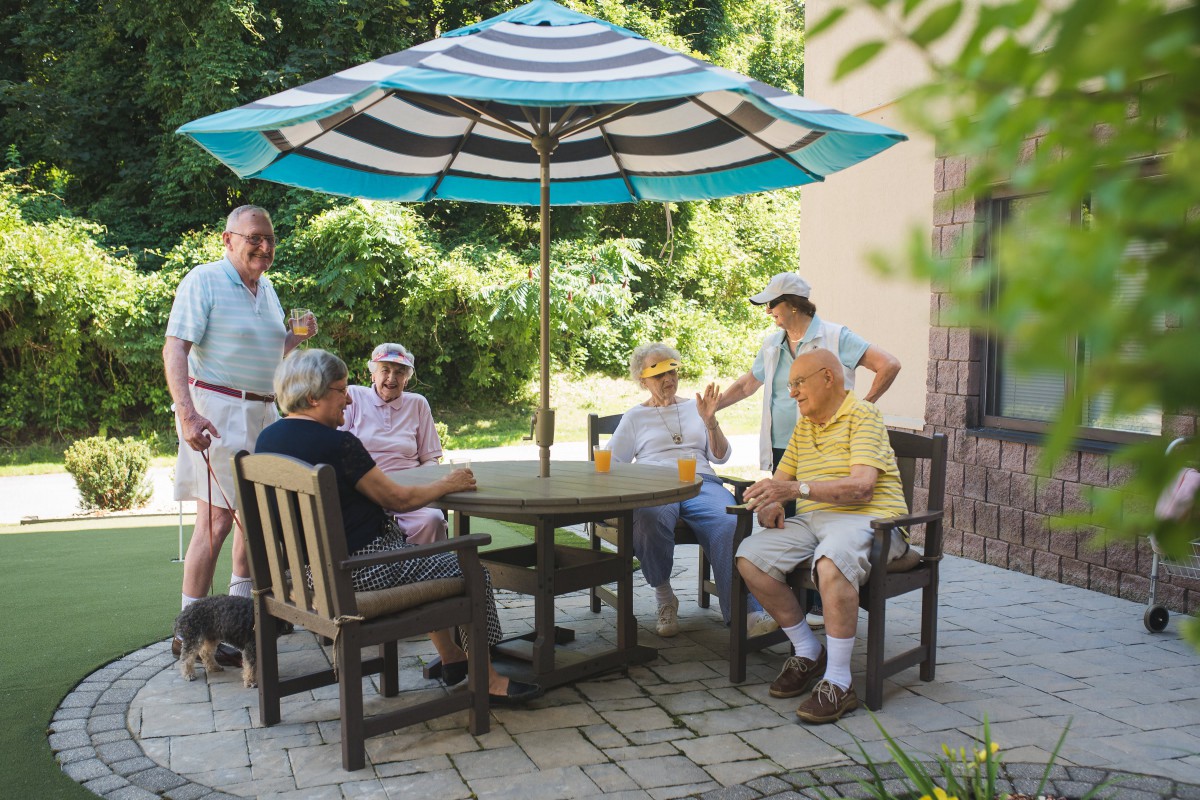 A group of seniors socializing outdoors on a patio under an umbrella.