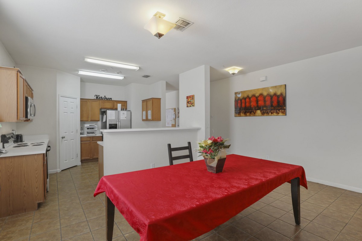 A cozy dining area with a red tablecloth and flowers, adjacent to a modern kitchen.