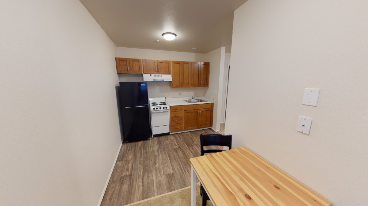 A compact apartment kitchen with wooden cabinets and a small dining area.