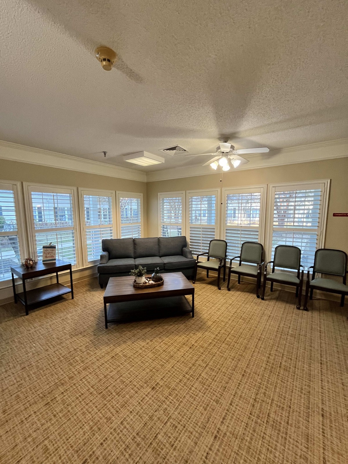 A cozy living room with a sofa, multiple chairs, and large windows allowing natural light.