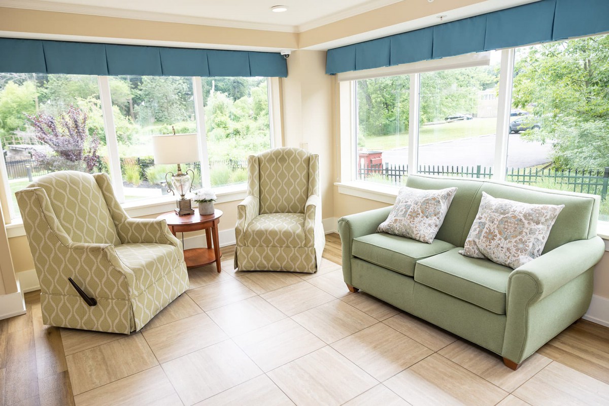A cozy living room with a sofa, two armchairs, and large windows providing natural light.