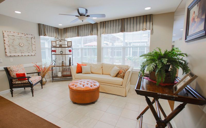 A cozy living room with a beige couch, round leather coffee table, and large windows adorned with curtains.