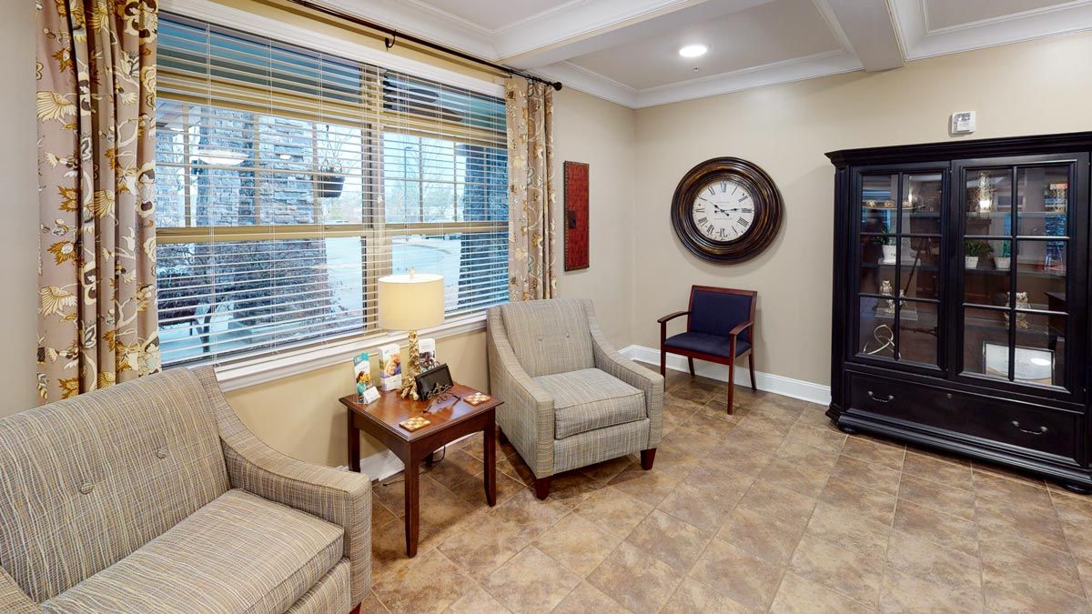 A cozy waiting room with comfortable seating, a large wall clock, and soft lighting from a table lamp.